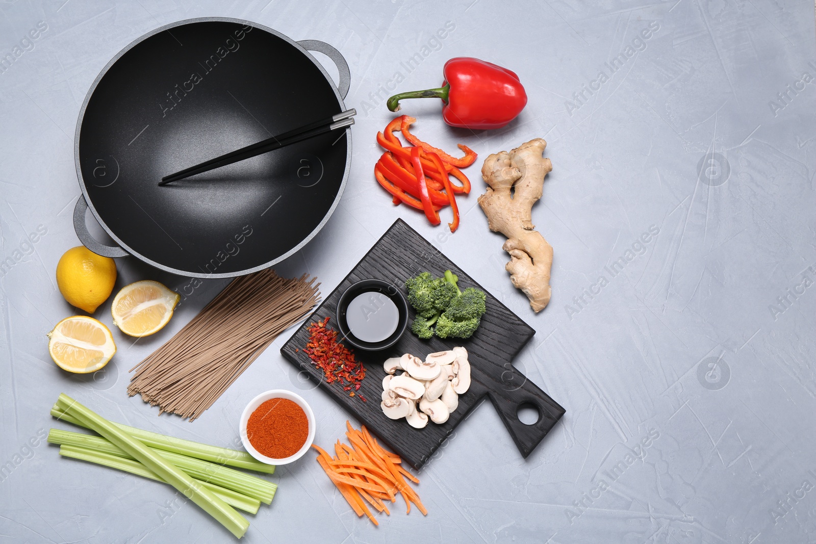 Photo of Wok, chopsticks and different products on grey table, flat lay. Space for text