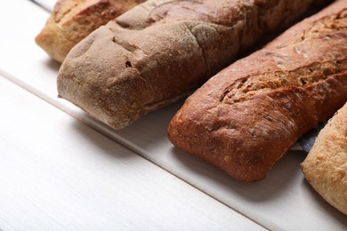 Photo of Different tasty baguettes on white wooden table, closeup