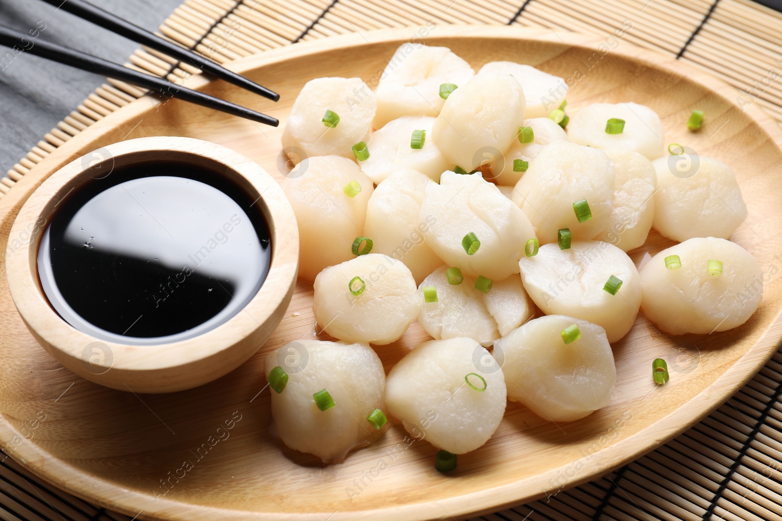 Photo of Raw scallops with green onion and soy sauce on dark table, closeup