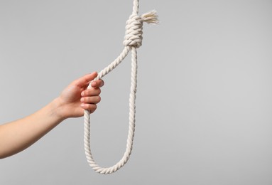 Photo of Woman holding rope noose on light grey background, closeup. Space for text