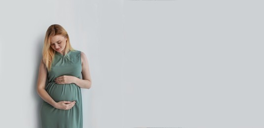 Image of Young pregnant woman touching belly on light background, space for text. Banner design