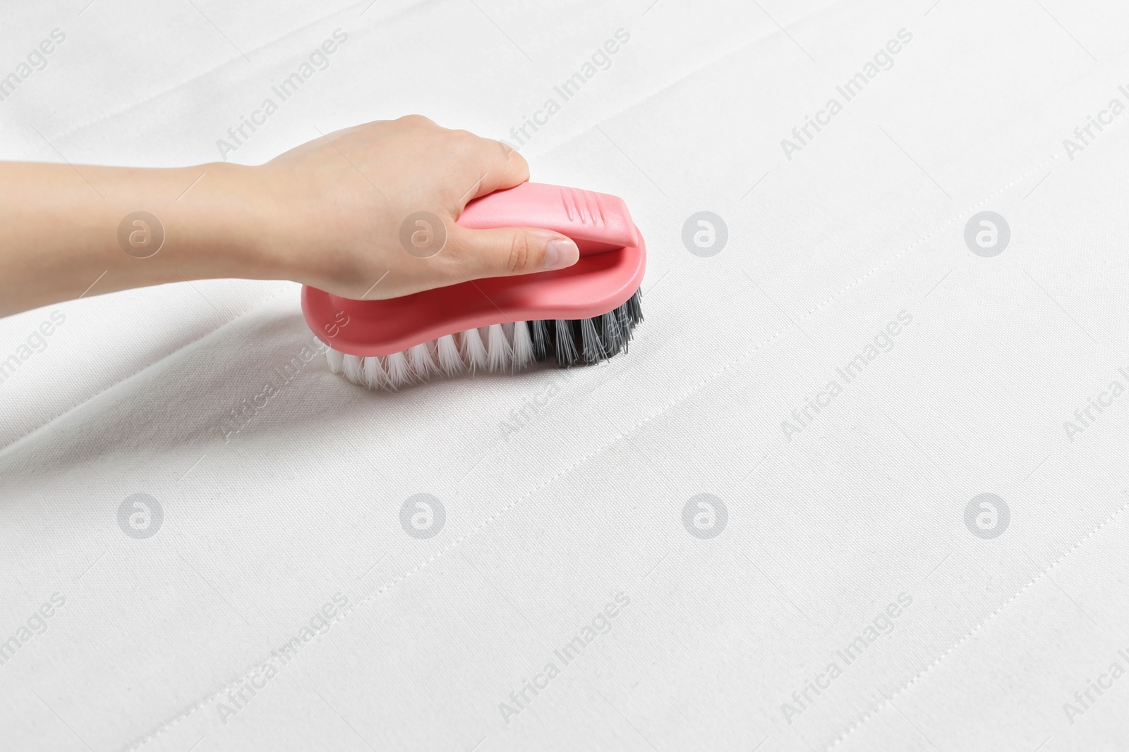 Photo of Woman cleaning white mattress with brush, closeup. Space for text