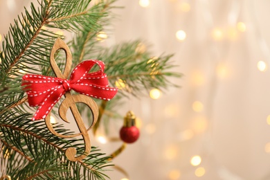 Photo of Fir tree branch with wooden treble clef on blurred background. Christmas music concept