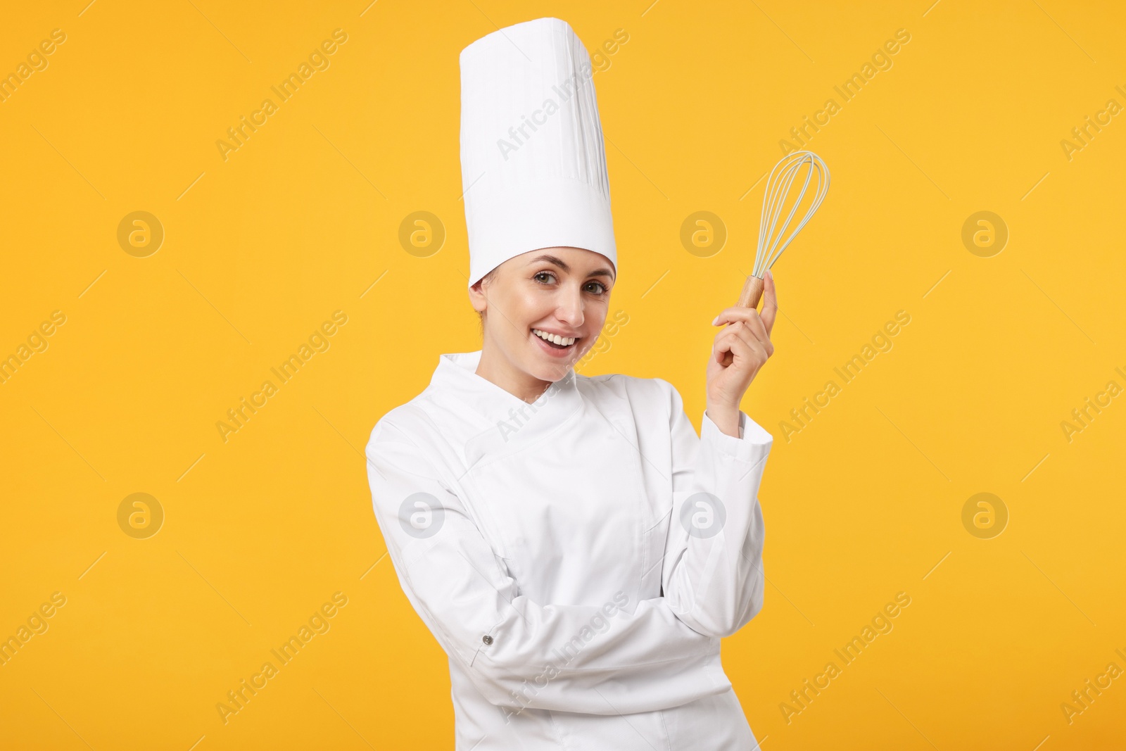 Photo of Happy professional confectioner in uniform holding whisk on yellow background