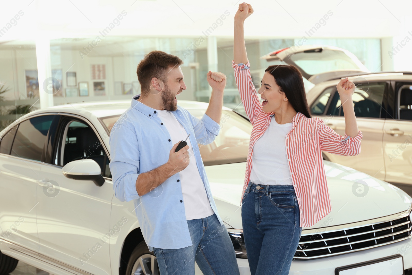 Photo of Happy couple with car key in modern auto dealership