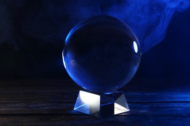 Magic crystal ball on wooden table against dark background. Making predictions