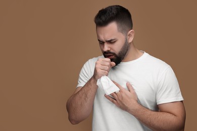 Sick man with tissue coughing on brown background, space for text
