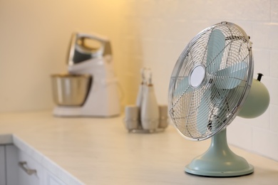 Photo of Modern electric fan on countertop in kitchen, space for text. Summer heat