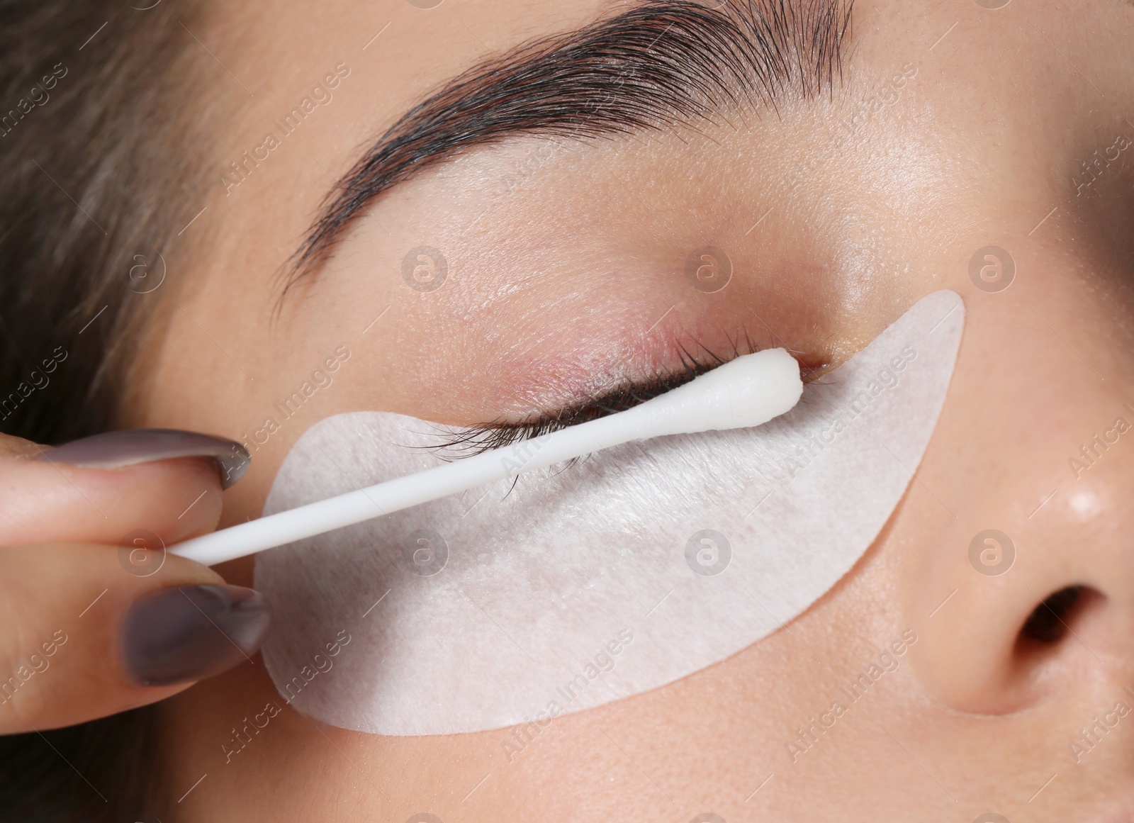 Photo of Young woman undergoing eyelashes extensions procedure, closeup