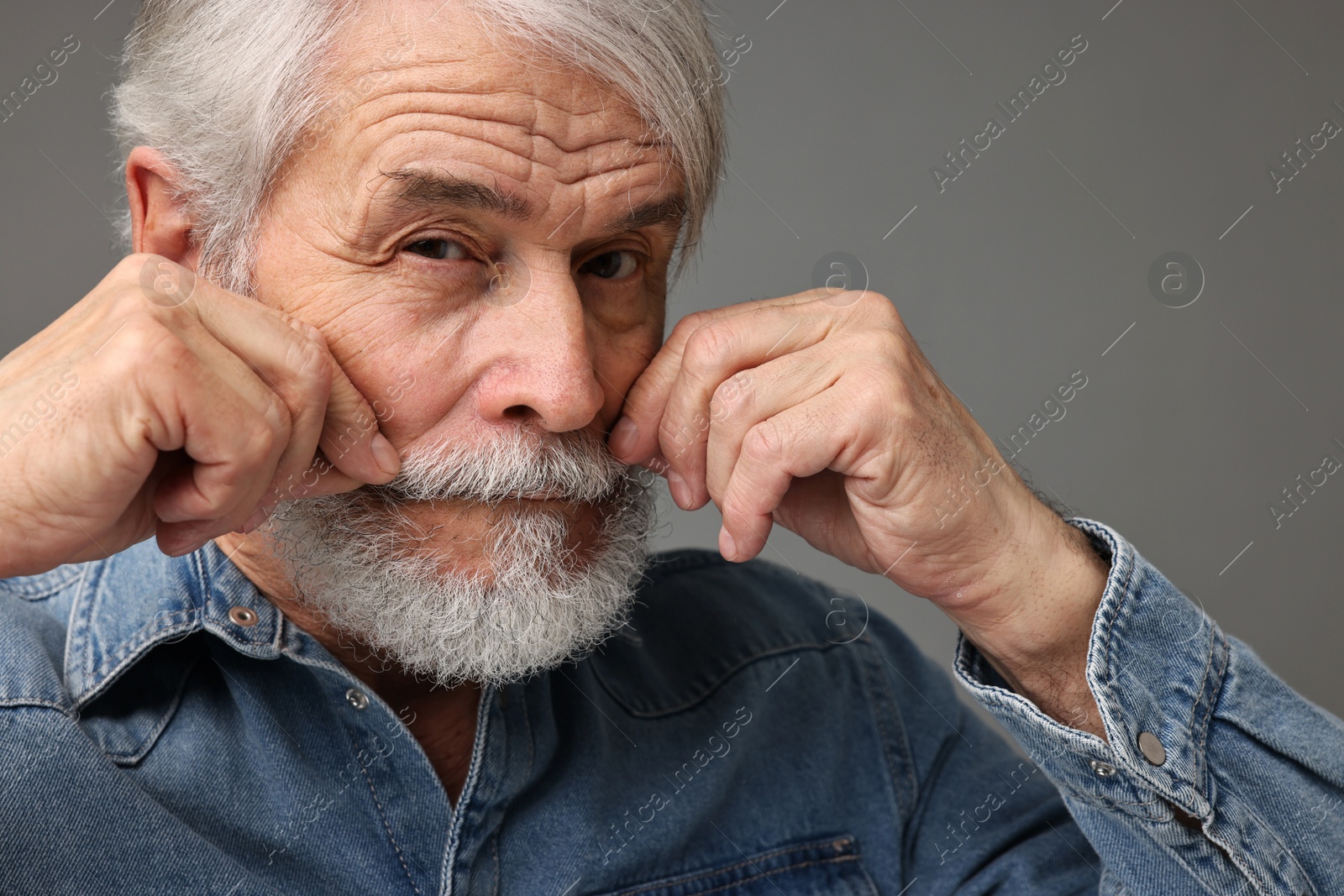 Photo of Senior man touching mustache on grey background