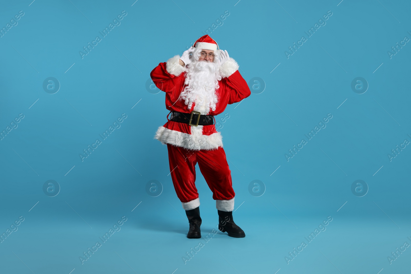 Photo of Merry Christmas. Santa Claus in headphones listening to music on light blue background