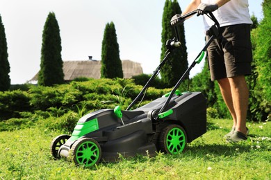 Man cutting grass with lawn mower in garden on sunny day, closeup