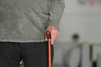 Photo of Elderly man with walking cane at home, closeup view of hand. Space for text