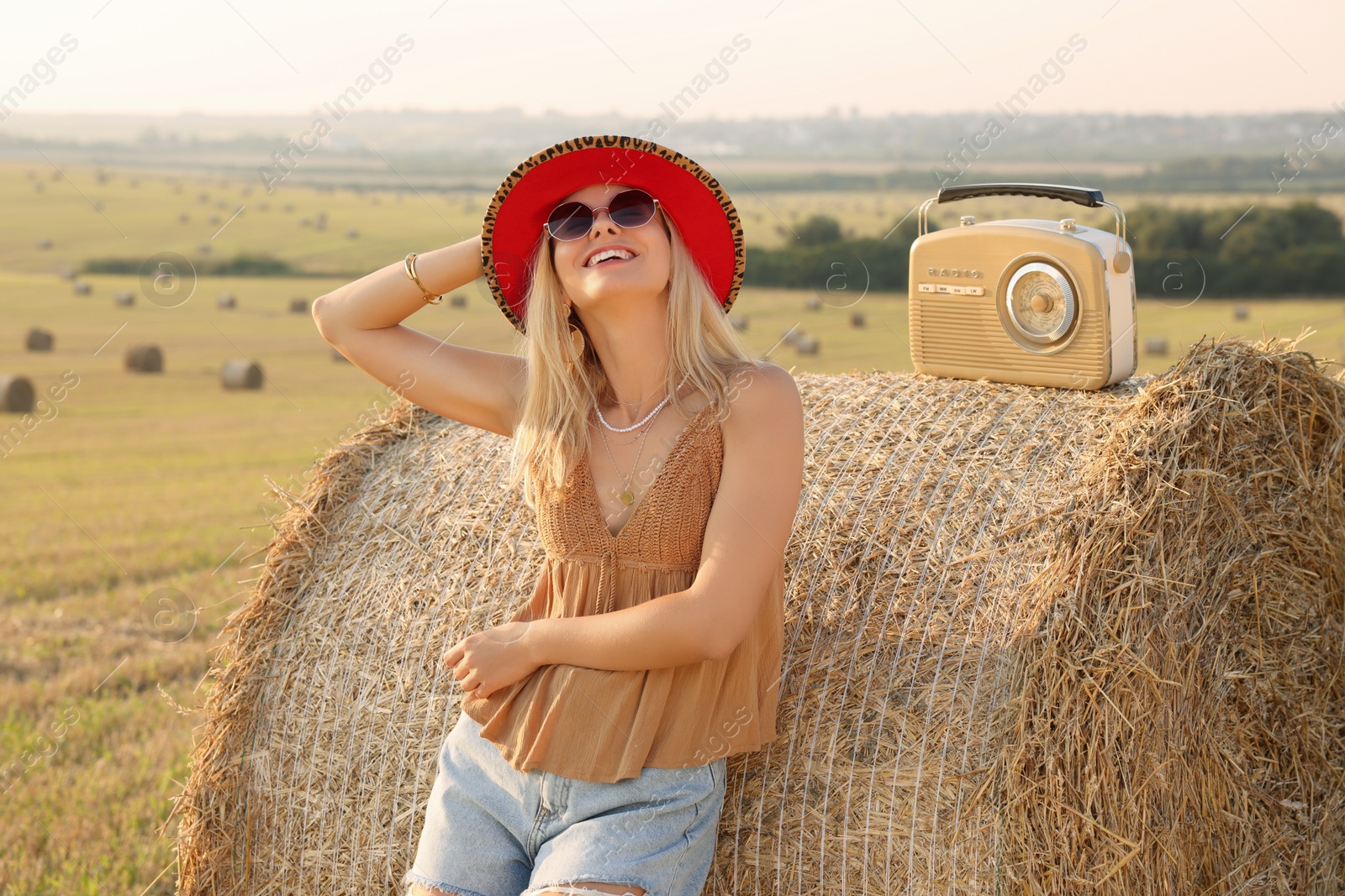 Photo of Happy hippie woman with receiver near hay bale in field