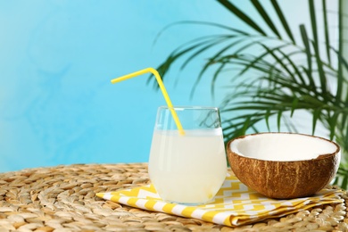 Composition with glass of coconut water on wicker table against blue background. Space for text