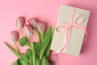 Beautiful gift box with bow and tulips on pink background, flat lay