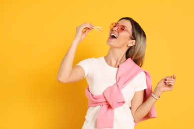 Photo of Young woman eating French fries on yellow background. Space for text