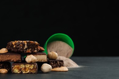 Photo of Different tasty energy bars, nuts and protein powder on black table, space for text