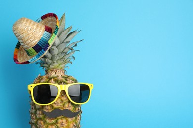 Photo of Pineapple with Mexican sombrero hat, sunglasses and fake mustache on light blue background, top view. Space for text