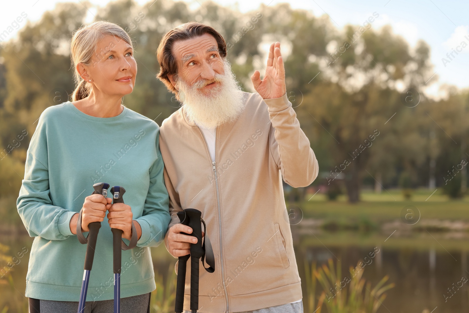 Photo of Senior man and woman with Nordic walking poles outdoors, space for text