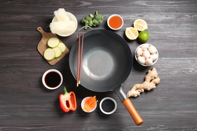 Photo of Empty iron wok and chopsticks surrounded by ingredients on dark grey wooden table, flat lay