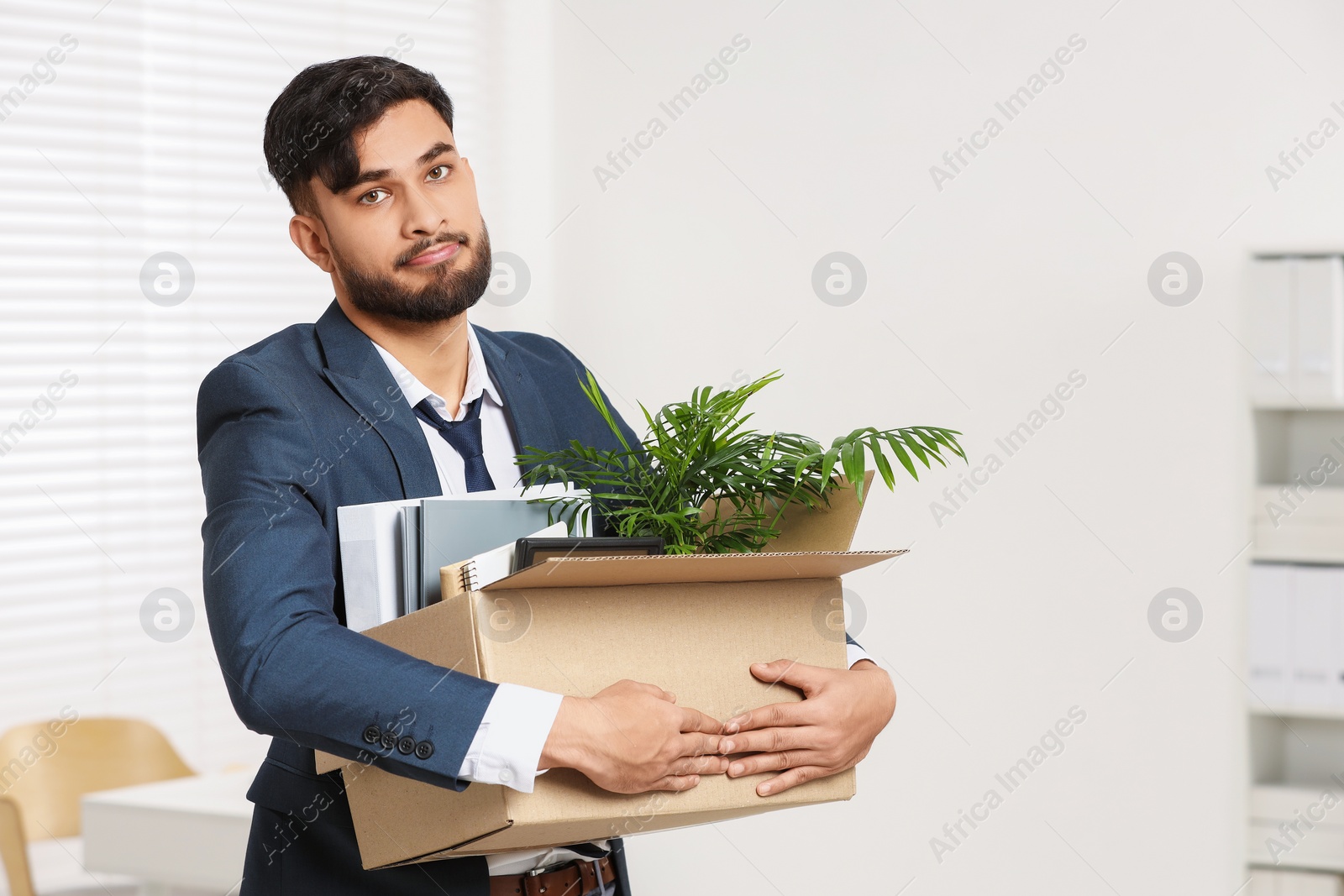 Photo of Unemployment problem. Frustrated man with box of personal belongings in office