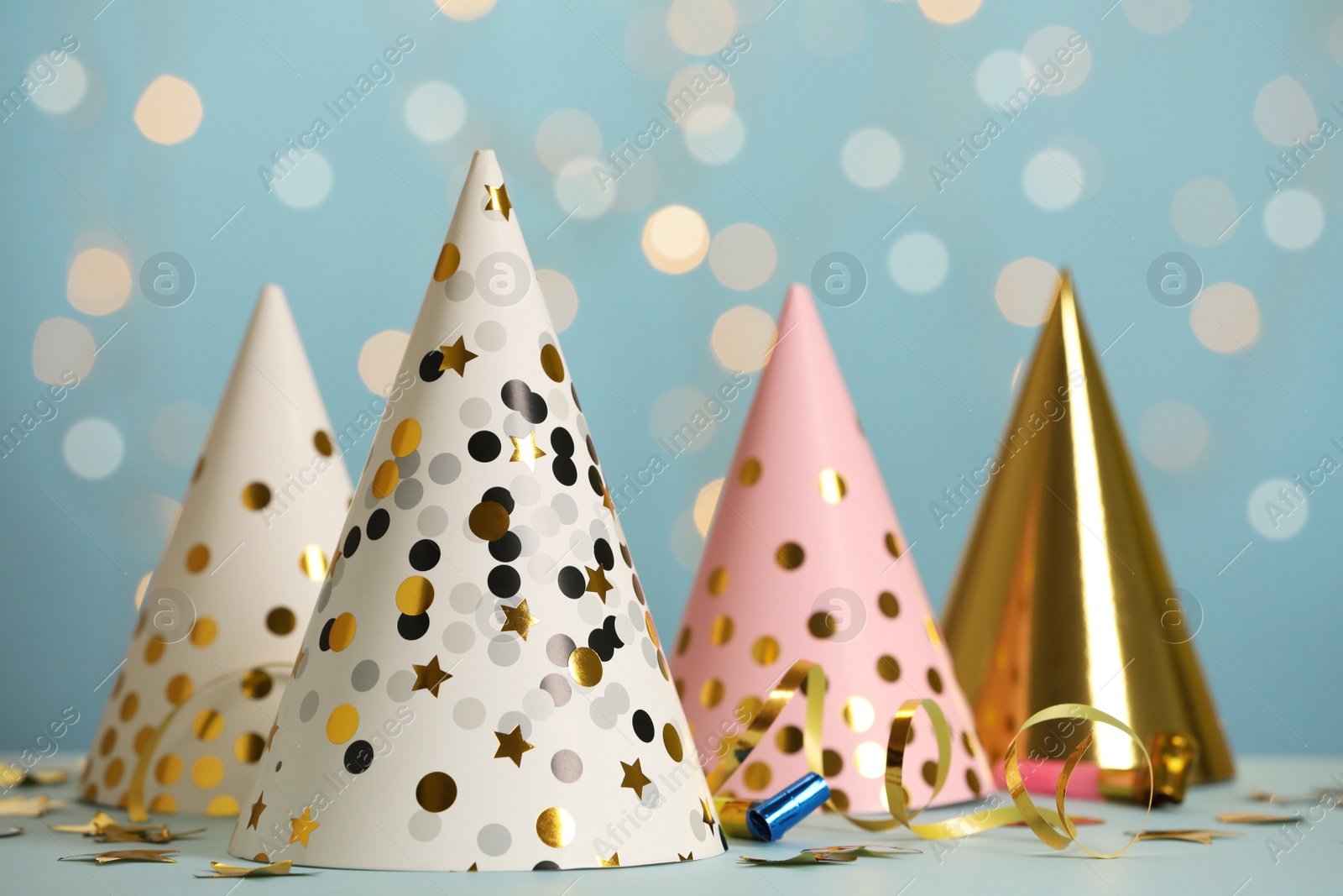 Photo of Party hats and festive items on table against blue background with blurred lights