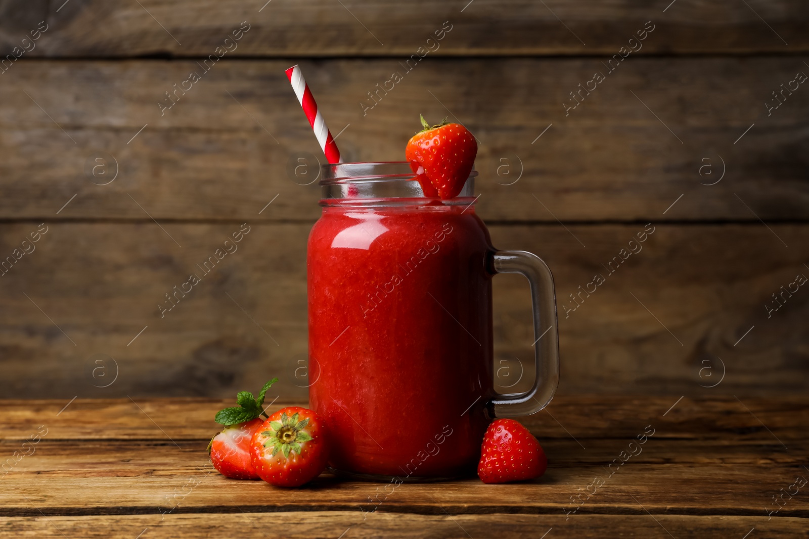 Photo of Mason jar with delicious strawberry smoothie and fresh berries on wooden table