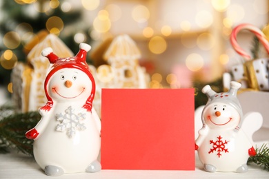 Photo of Decorative snowman near blank red card on table, space for text