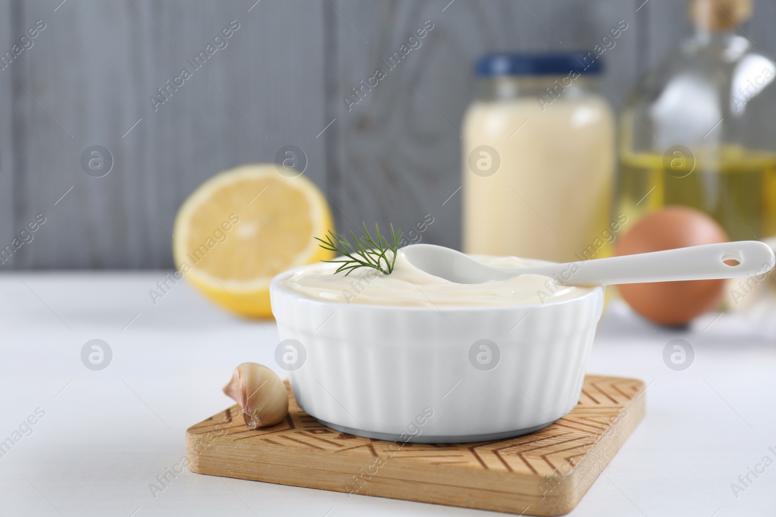 Photo of Fresh mayonnaise sauce in bowl and ingredients on white table