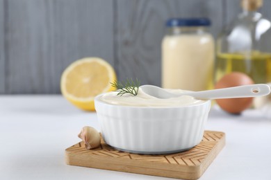 Photo of Fresh mayonnaise sauce in bowl and ingredients on white table