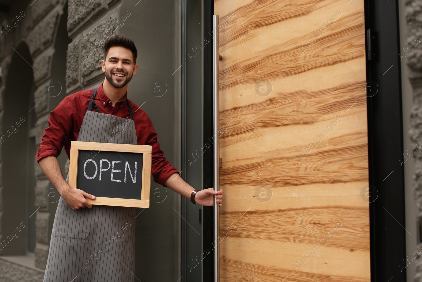 Photo of Young male business owner holding OPEN sign near his cafe. Space for text