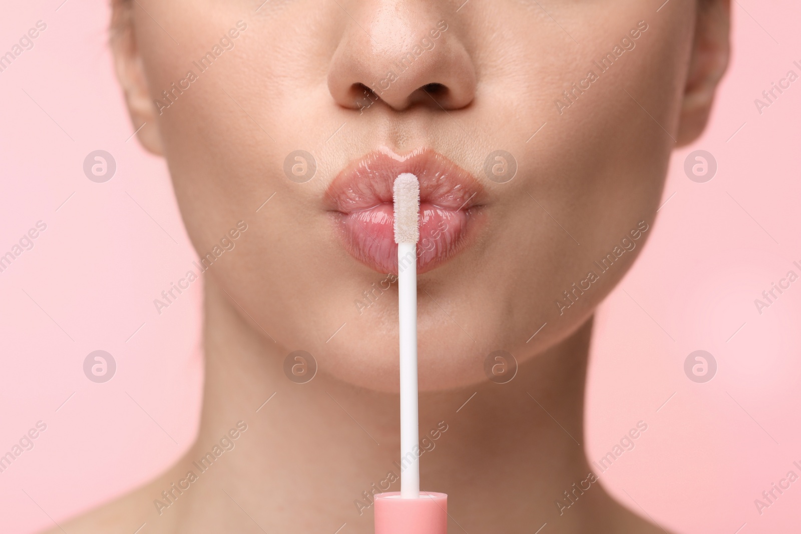 Photo of Woman with beautiful lip gloss and applicator on pink background, closeup