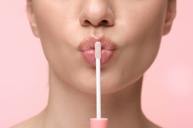 Woman with beautiful lip gloss and applicator on pink background, closeup