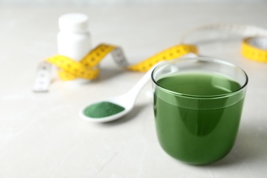 Photo of Glass of spirulina drink and powder on table, space for text