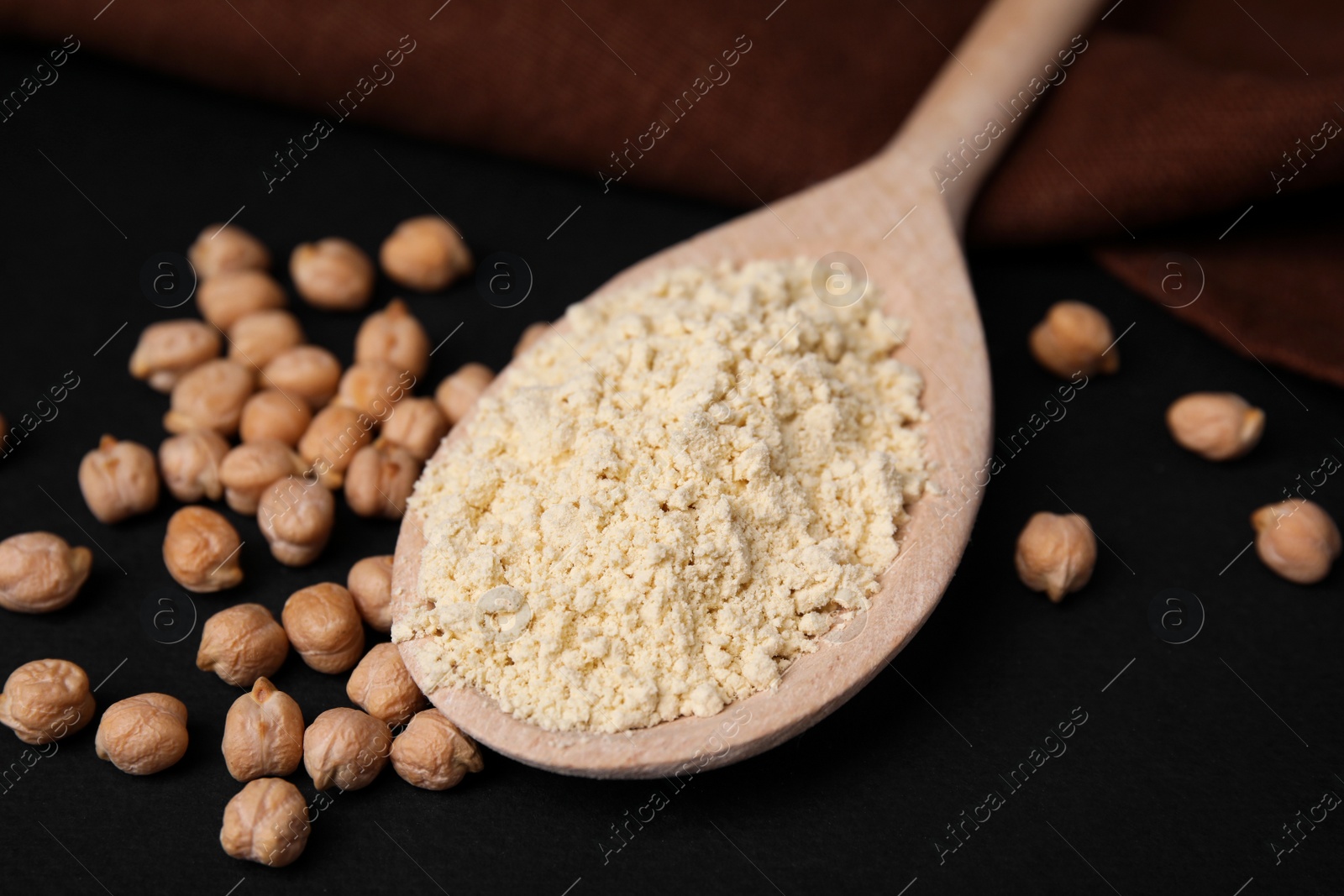 Photo of Spoon with chickpea flour and seeds on black table, closeup