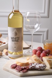 Photo of Bottle of white wine, glass and snacks on table