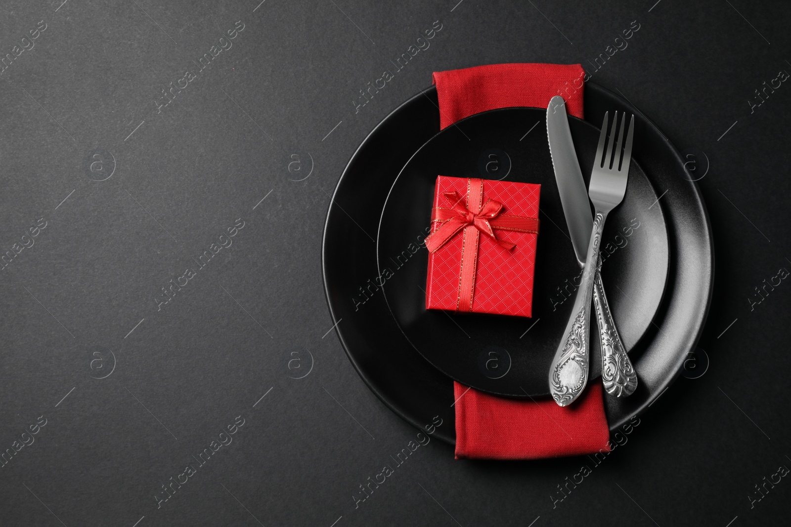 Photo of Dishware, cutlery and gift box on black table for romantic dinner, top view. Space for text