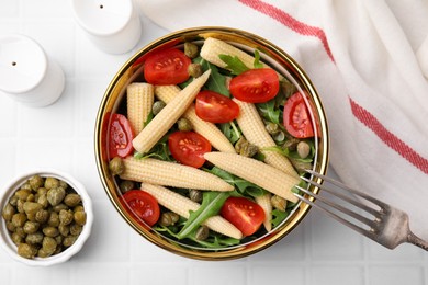 Photo of Tasty baby corn with tomatoes, arugula and capers on white tiled table, flat lay