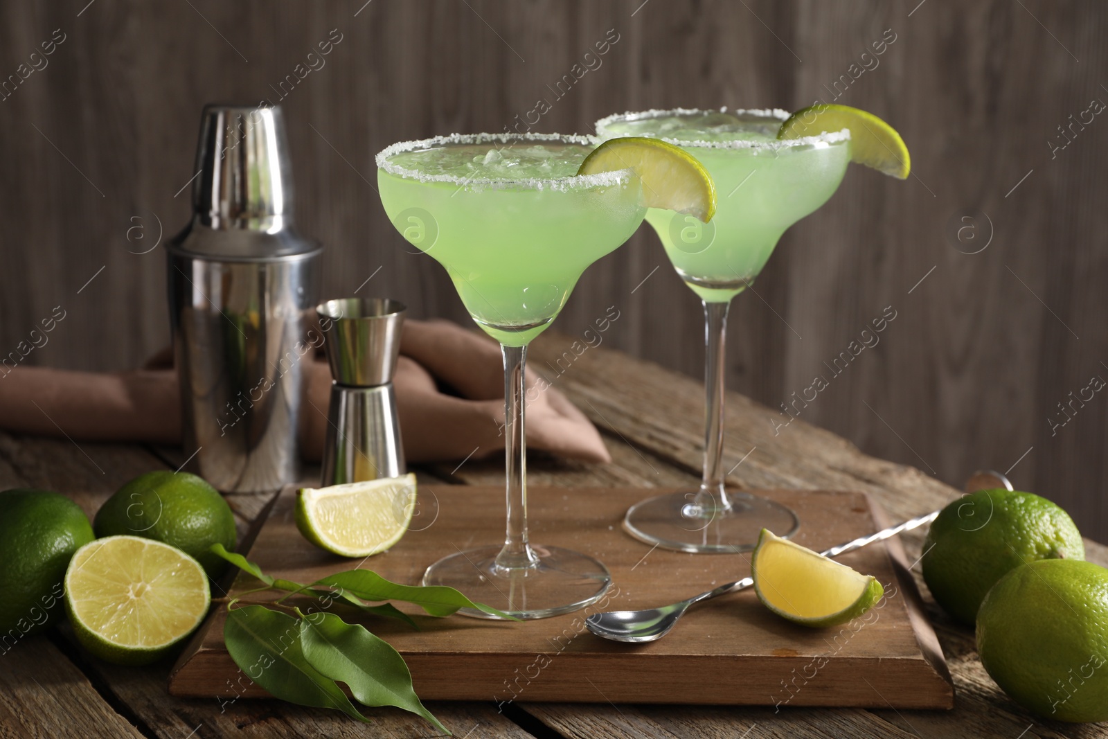 Photo of Delicious Margarita cocktail in glasses, limes and bartender equipment on wooden table