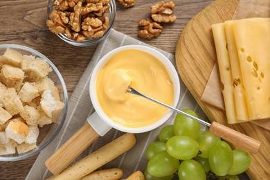 Flat lay composition with pot of tasty cheese fondue on wooden table