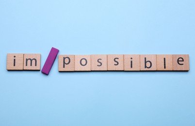 Photo of Motivation concept. Changing word from Impossible into Possible by adding slash symbol on light blue background, flat lay