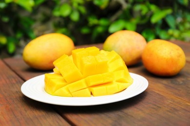 Photo of Delicious ripe cut and whole mangos on wooden table outdoors