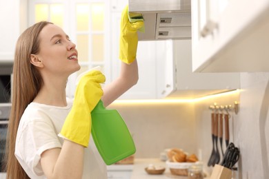 Woman with spray bottle and microfiber cloth cleaning kitchen hood at home