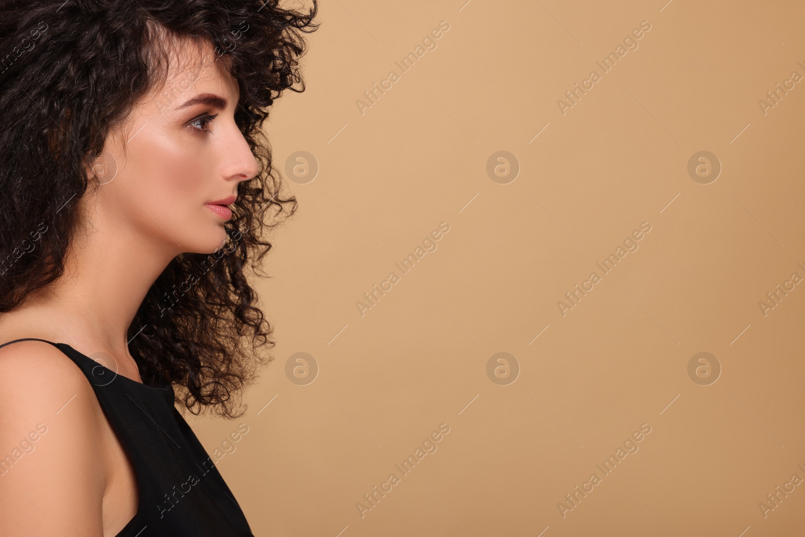 Photo of Beautiful young woman with long curly hair on beige background. Space for text