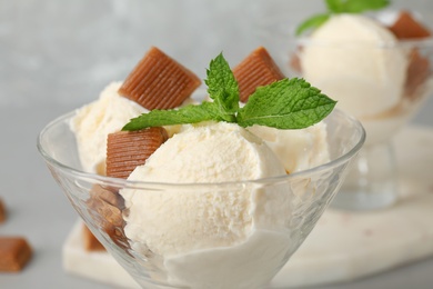 Photo of Glass dish of delicious ice cream with caramel candies and mint on table, closeup