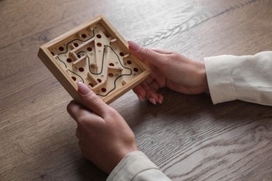 Photo of Woman holding wooden toy maze with metal ball at table, closeup