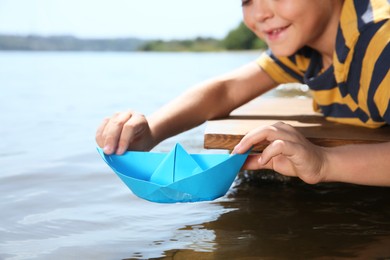 Photo of Little boy playing with paper boat on pier near river, closeup