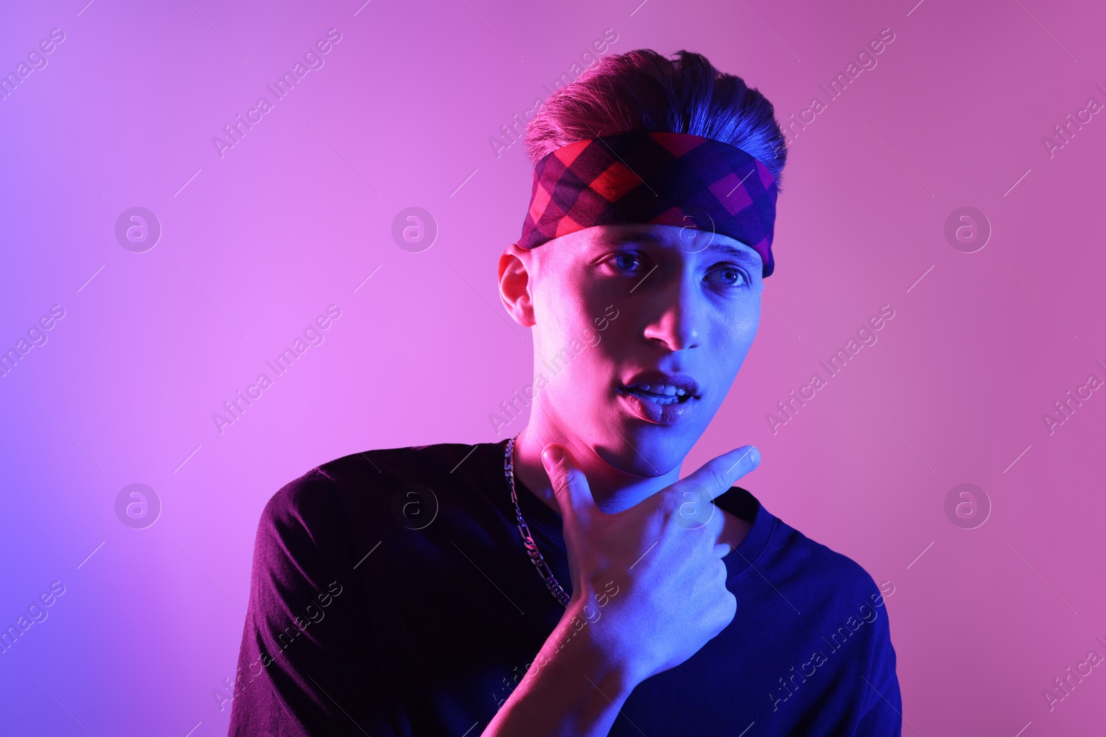 Photo of Stylish young man on color background in neon lights. Space for text