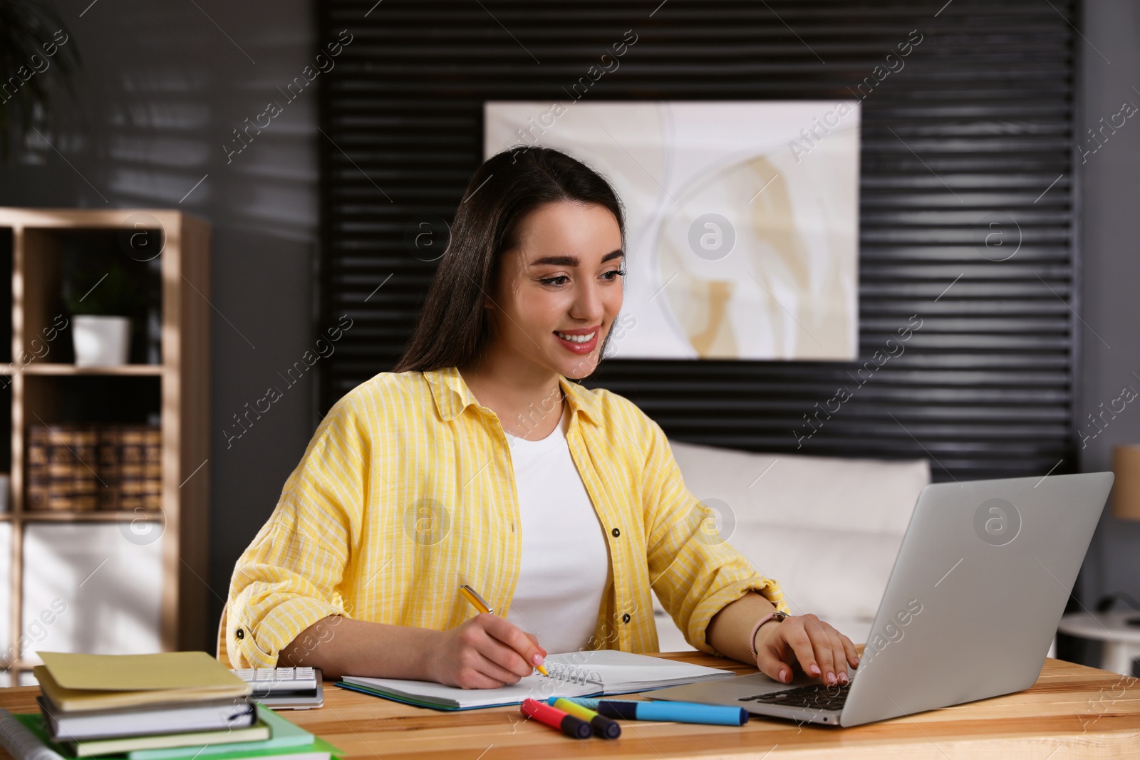 Photo of Young woman watching webinar at table in room